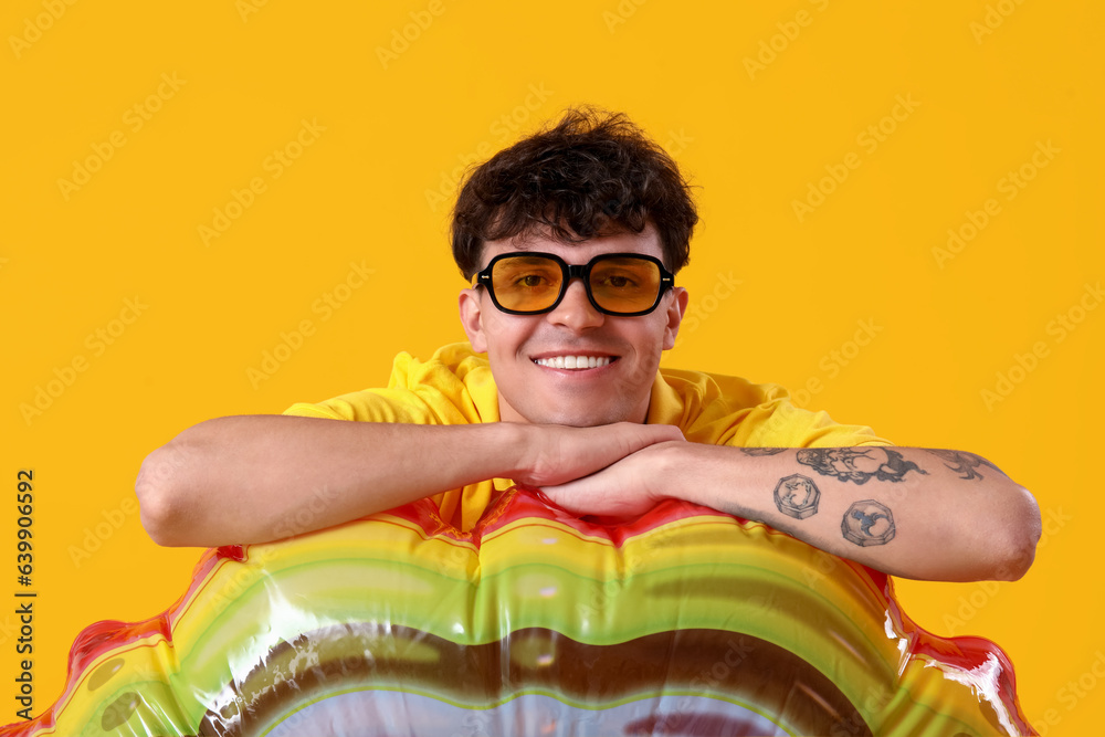 Young man in sunglasses with inflatable ring on yellow background