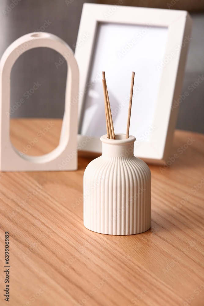 Bottle of reed diffuser and blank frame on table in room, closeup