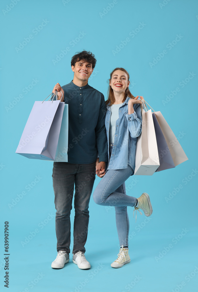 Happy young couple with shopping bags on blue background