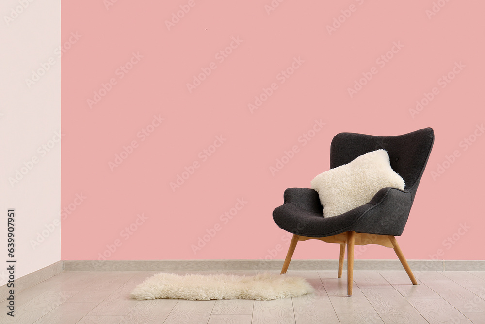 Grey armchair with cushion near pink wall