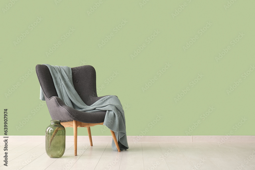 Grey armchair with blanket and vase near green wall