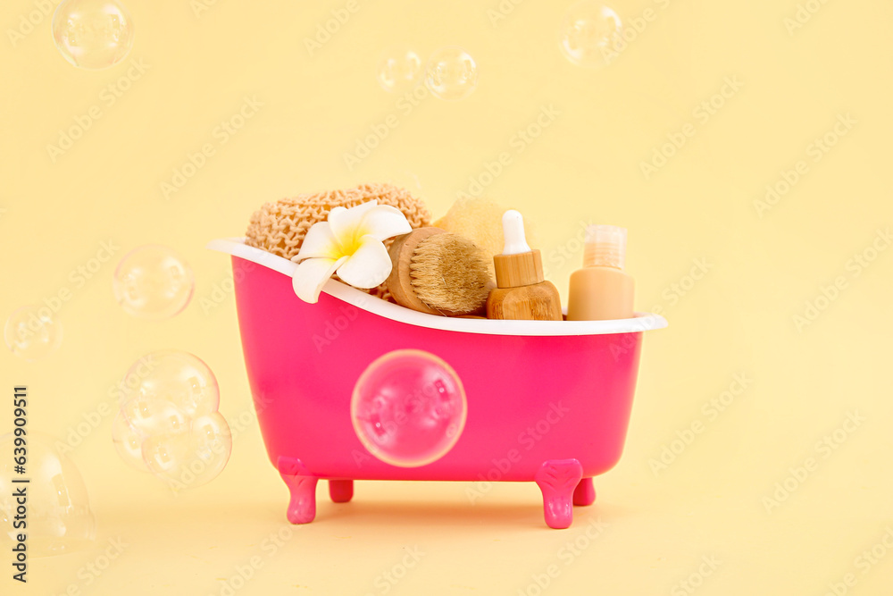 Small bathtub with different bath supplies and soap bubbles on color background