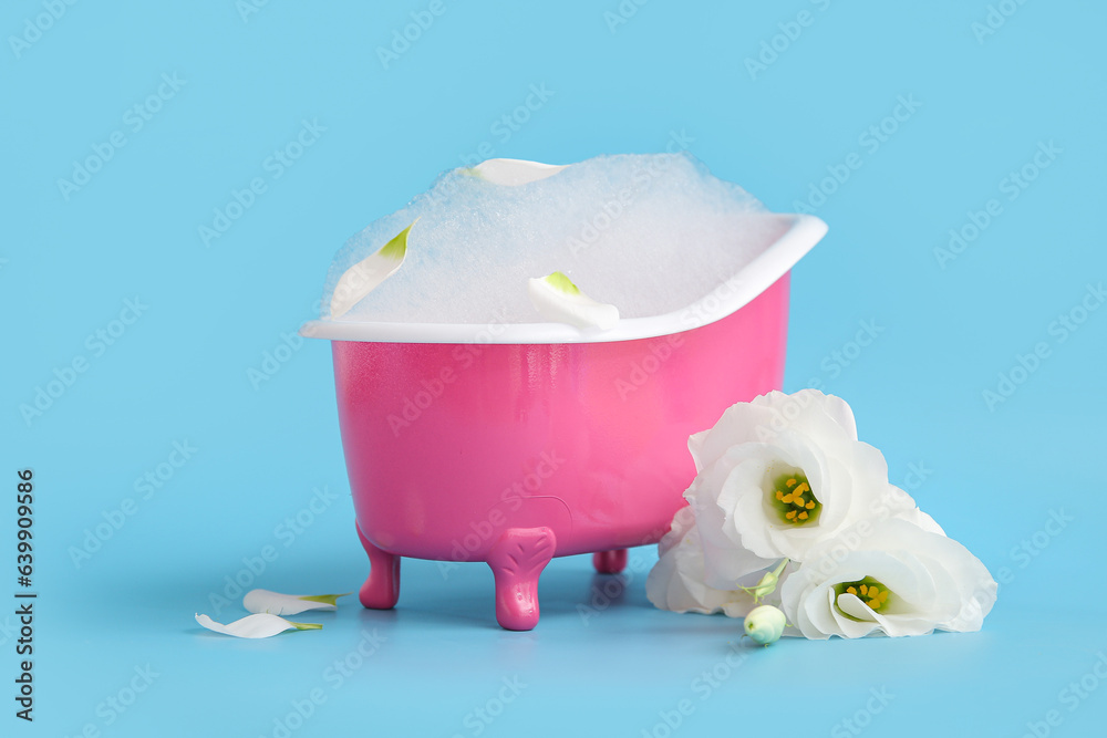 Small bathtub with soap foam and beautiful eustoma flowers on color background