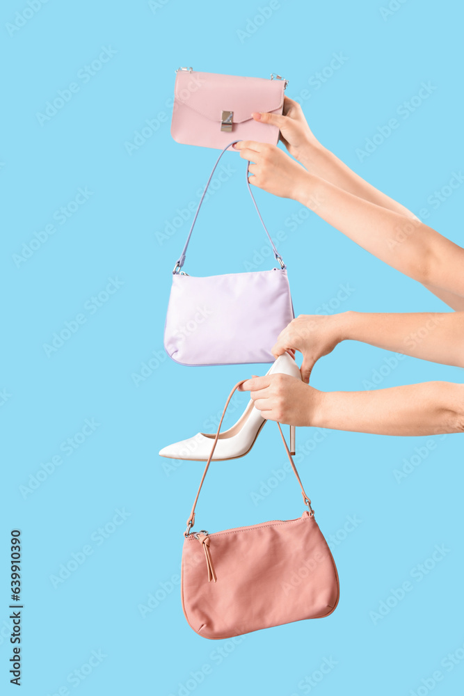 Female hands holding stylish womens bags and shoe on blue background