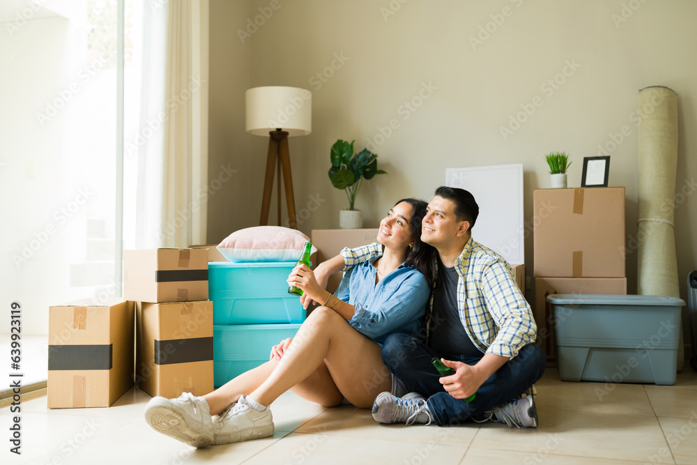 Latin couple drinking beer and relaxing after moving boxes in their new apartment