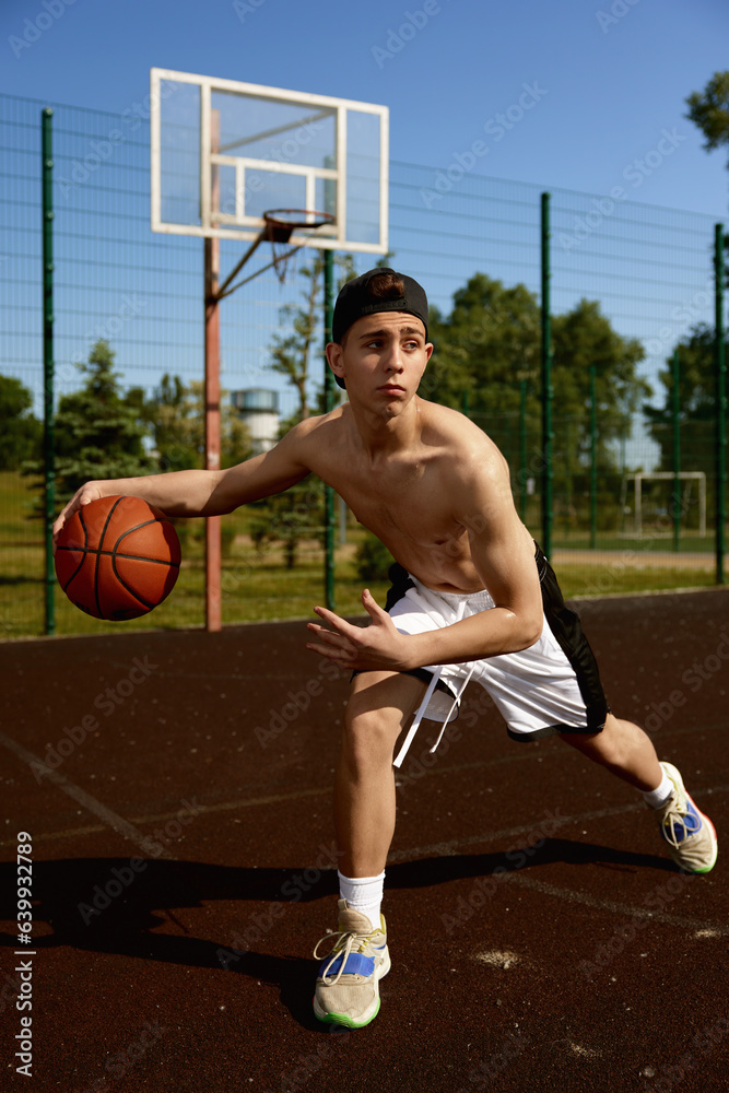 Active teenager basketball player practicing with ball on street court