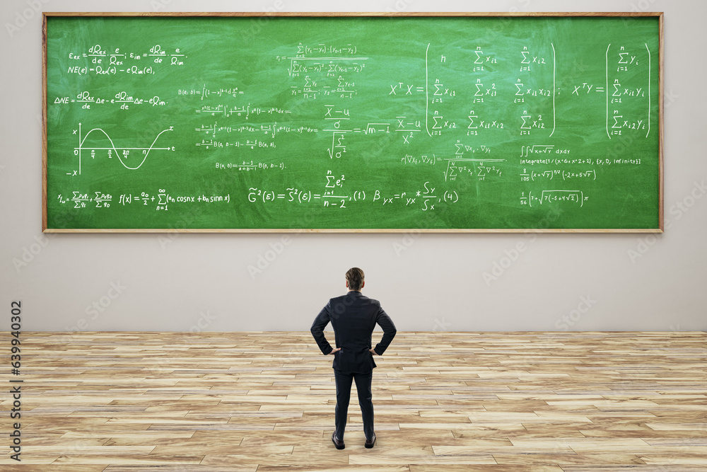 Thoughtful young european businessman standing in modern classroom interior with formulas on green c