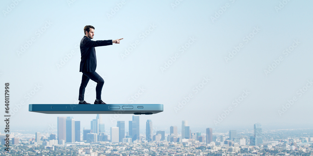 User experiences for mobile concepts. Young man pointing forward on huge flying smartphone on wide b