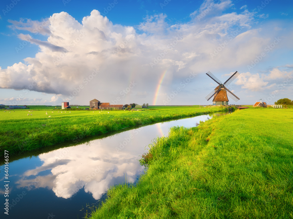 Landscape with windmill and rainbow. A huge cloud after a storm. Reflections on the surface of the w