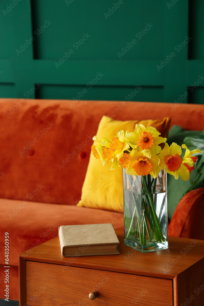 Vase with narcissus flowers and book on end table in living room