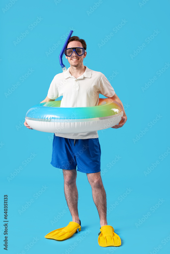 Young man in snorkeling mask with inflatable ring on blue background