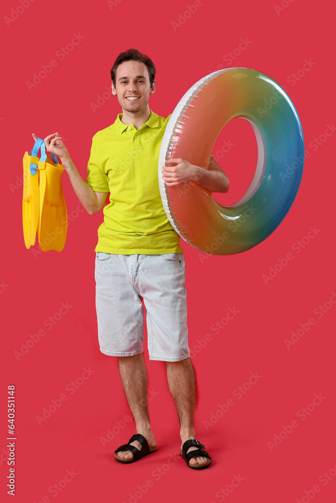 Young man with inflatable ring and flippers on red background