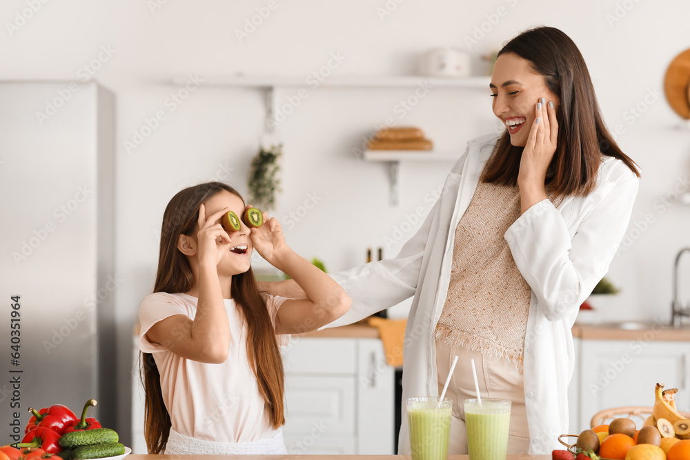 Little girl with her pregnant mother drinking green smoothie in kitchen