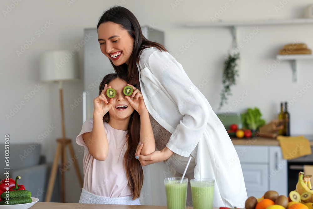 Little girl with her pregnant mother drinking green smoothie in kitchen