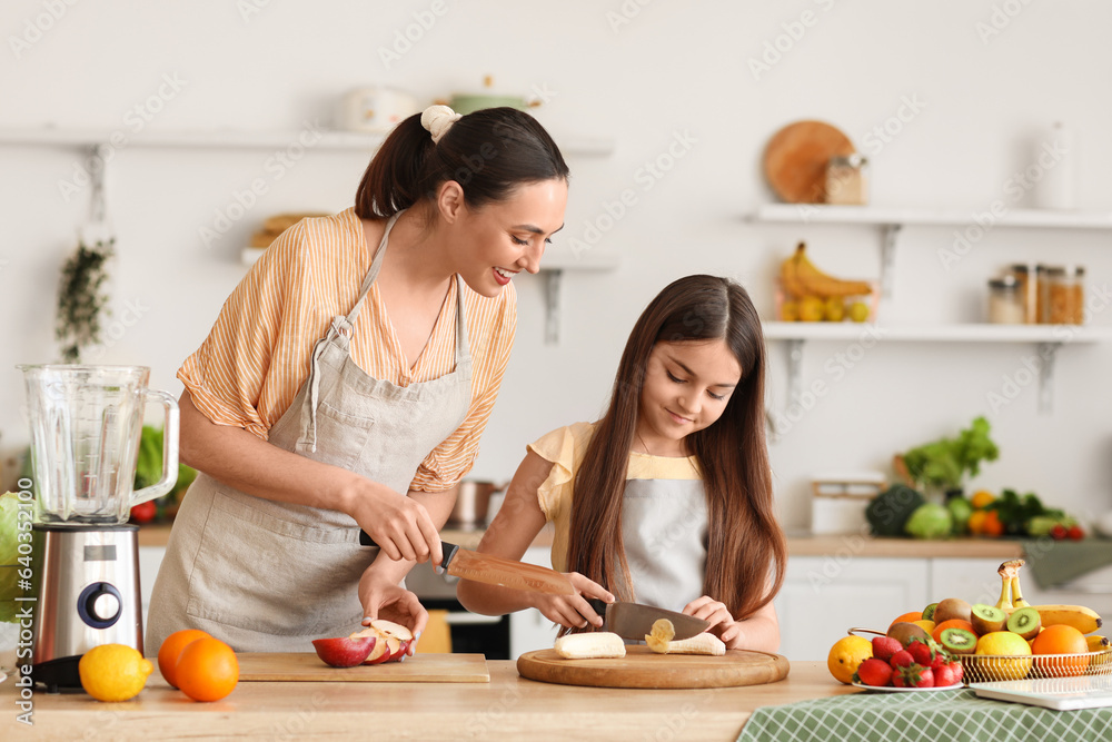 Little girl with her mother cutting fruits for smoothie in kitchen