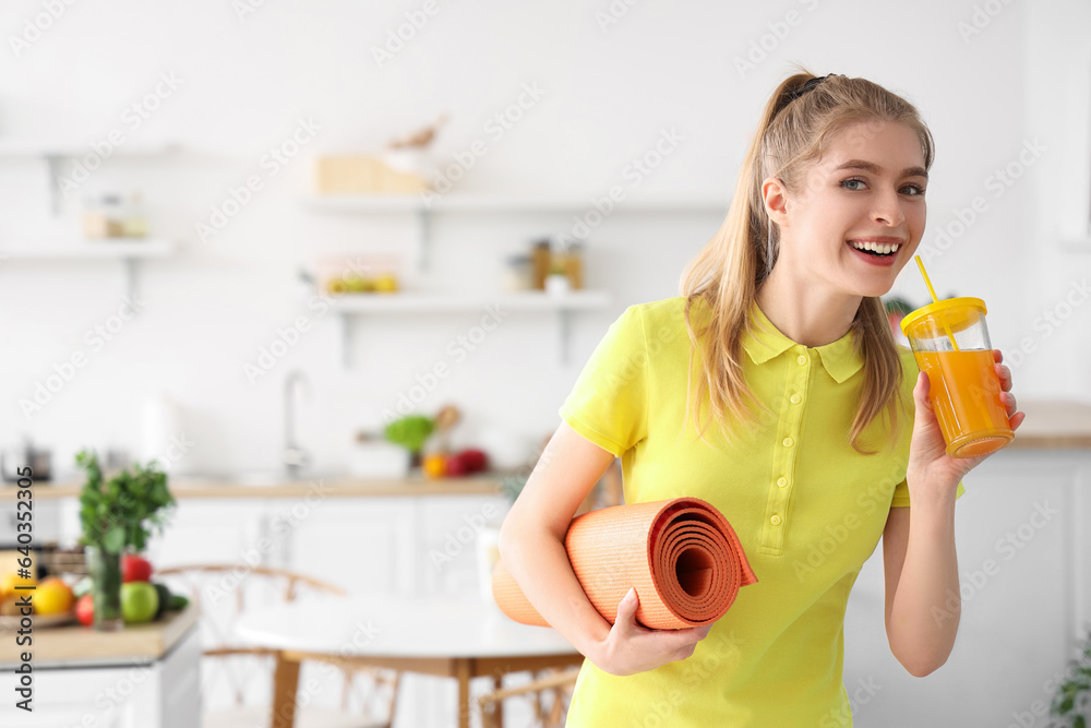 Sporty young woman with fitness mat drinking vegetable juice in kitchen