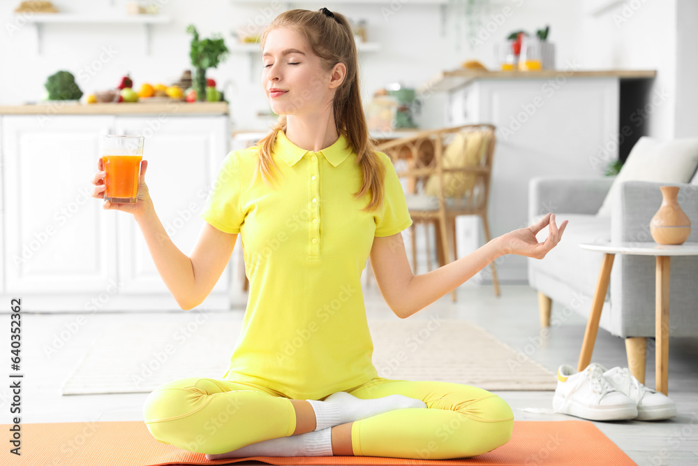 Sporty young woman with glass of vegetable juice meditating in kitchen