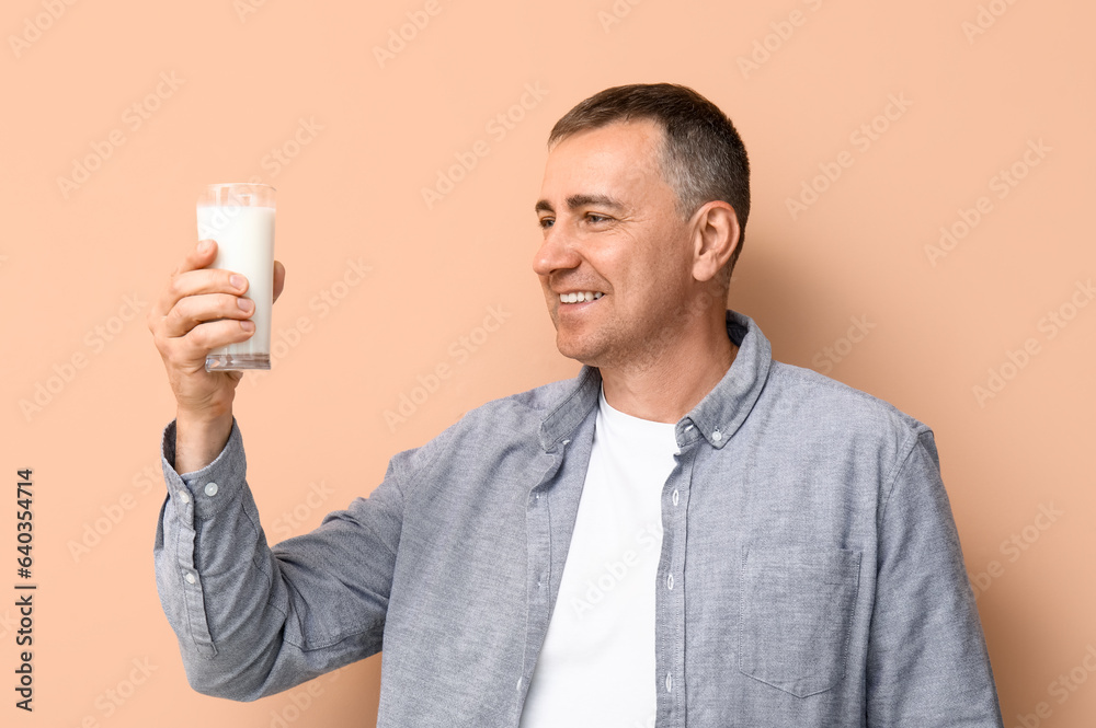 Mature man with glass of milk on beige background