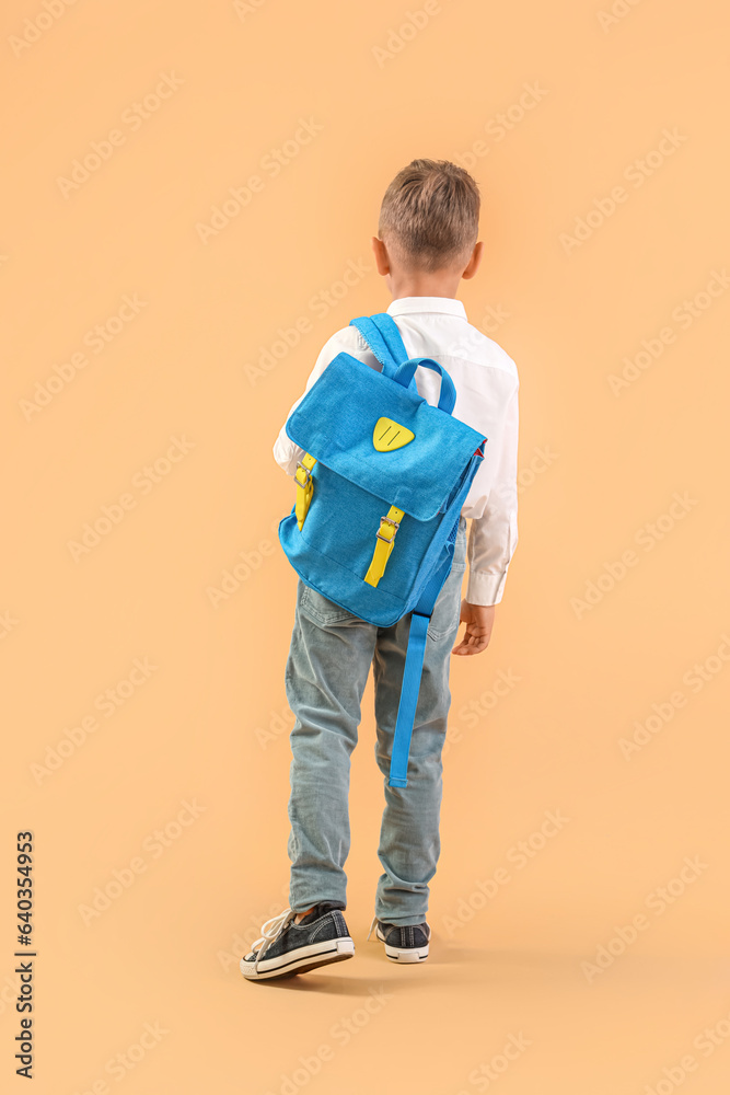 Little schoolboy with blue backpack on orange background, back view