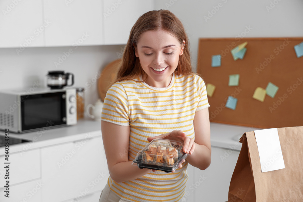 Happy young woman with sushi and paper bag in kitchen