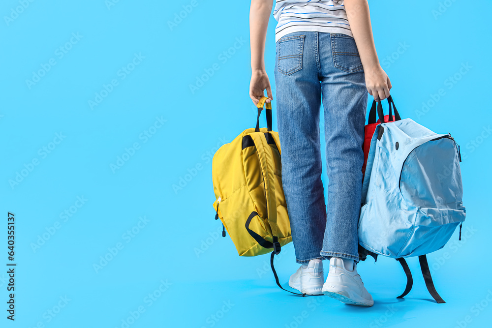 Little schoolboy with backpacks on blue background, back view