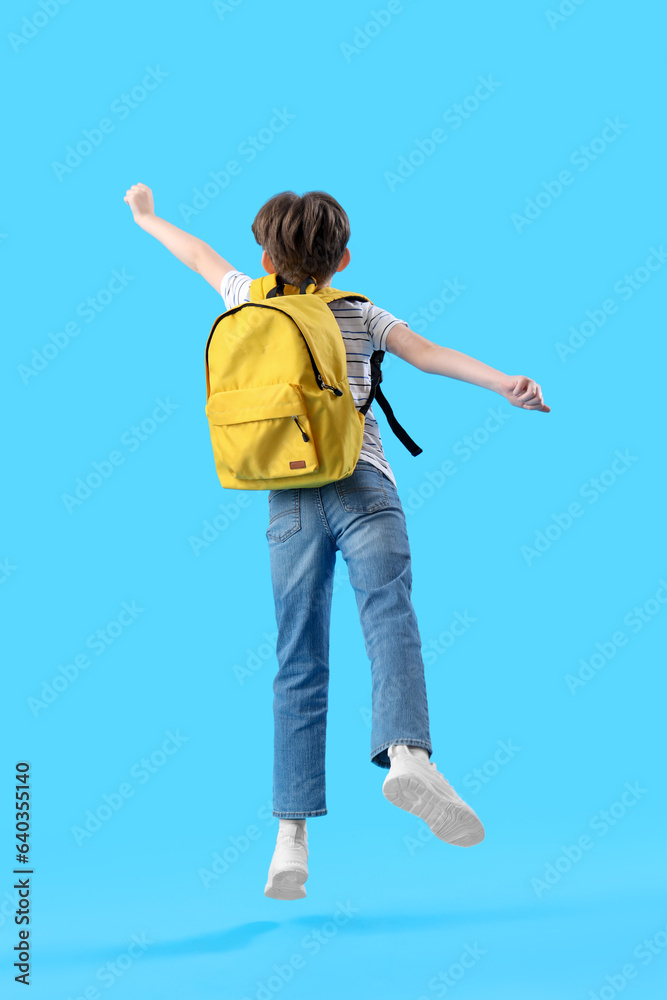 Jumping little boy with schoolbag on blue background, back view