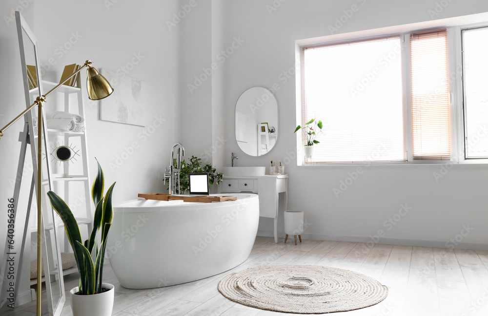 Interior of light bathroom with bathtub, dressing table and shelving unit