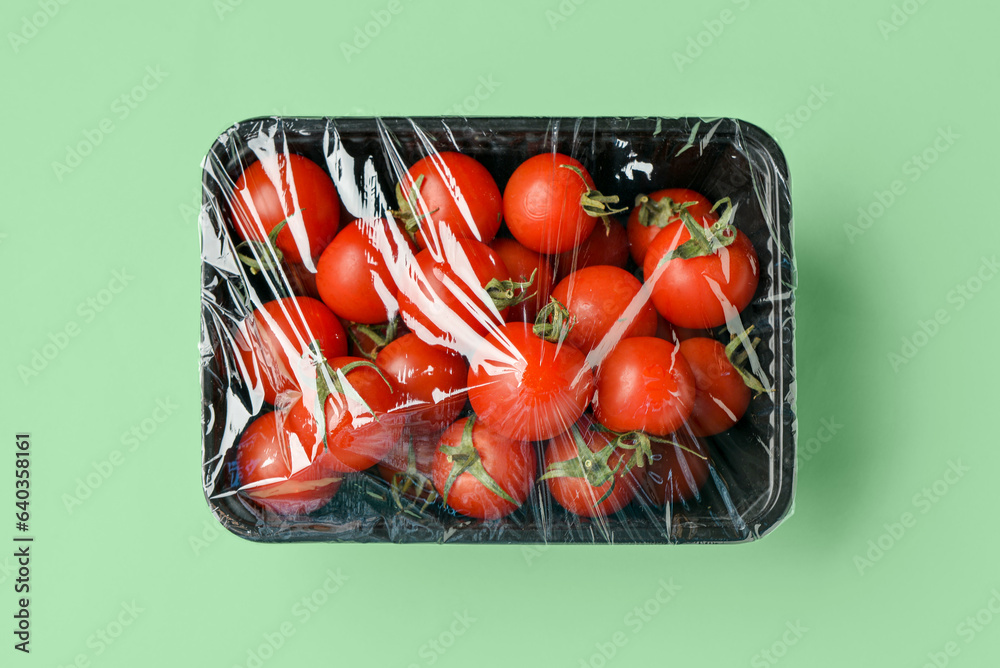 Plastic container of fresh tomatoes wrapped with stretch wrap on color background