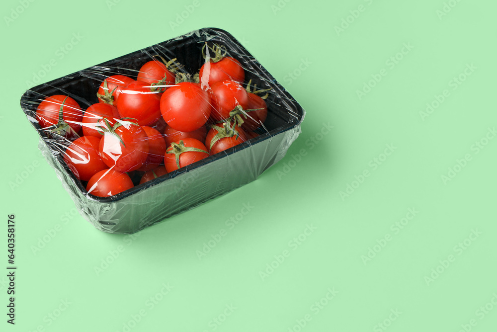 Plastic container of fresh tomatoes wrapped with stretch wrap on color background