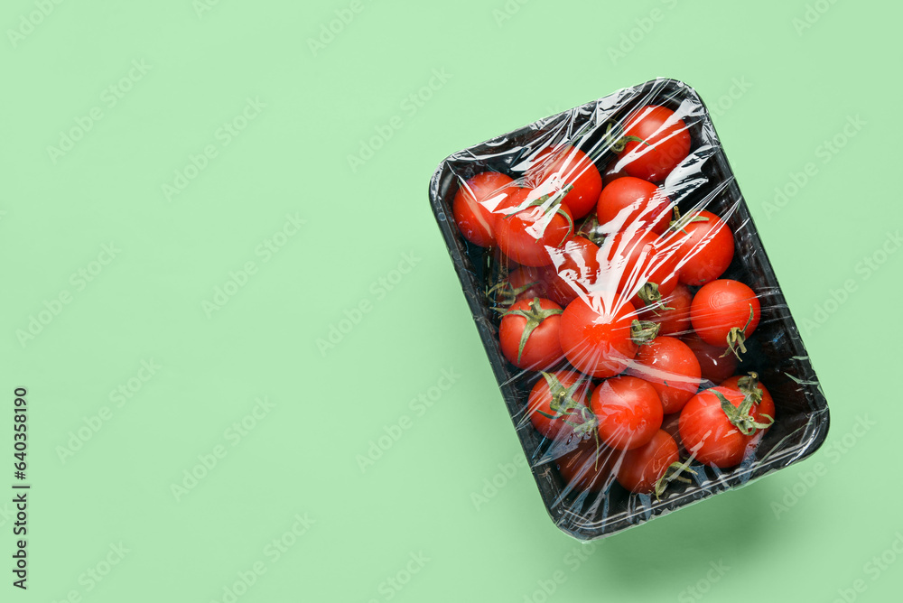 Plastic container of fresh tomatoes wrapped with stretch wrap on color background