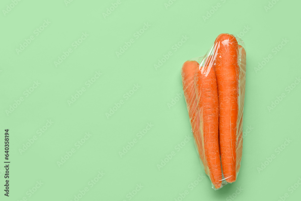 Fresh carrot wrapped in stretch wrap on color background