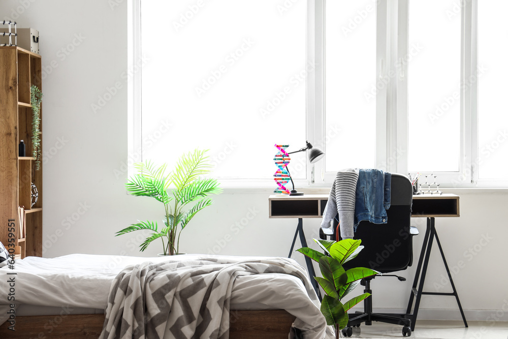 Interior of childrens bedroom with cozy bed, shelving unit, desk and houseplants