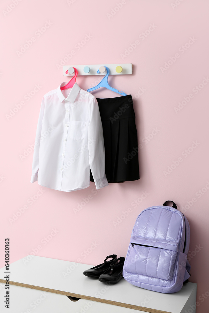 Stylish school uniform hanging on rack with backpack against pink wall