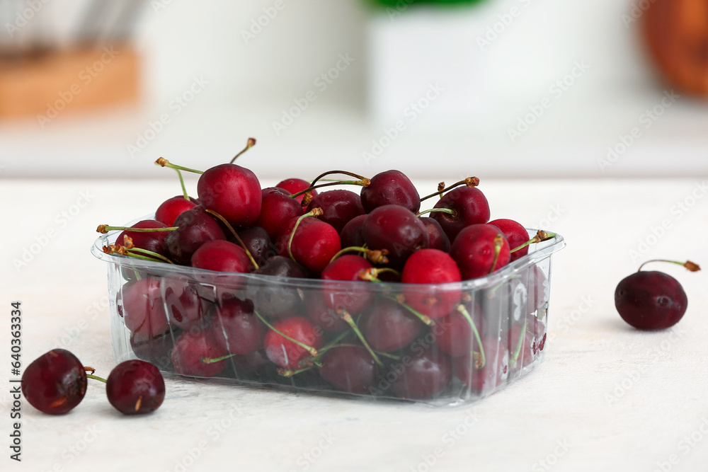 Plastic container with ripe cherries on table in kitchen