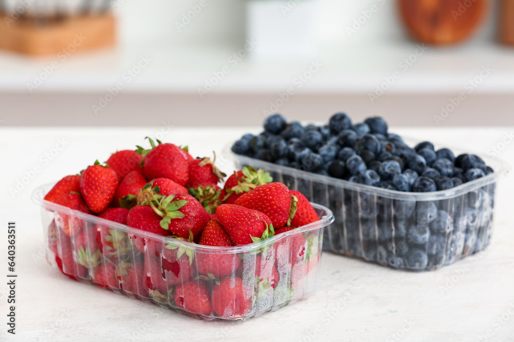 Plastic containers with ripe berries on table in kitchen