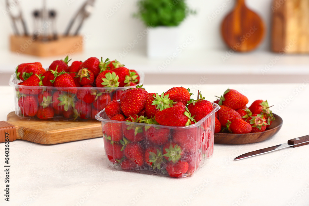 Plastic containers with ripe strawberries on table in kitchen