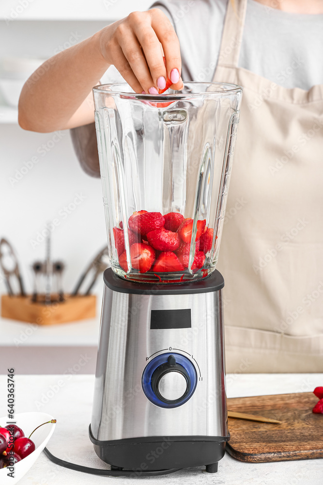 Woman preparing tasty strawberry smoothie with blender at table in kitchen