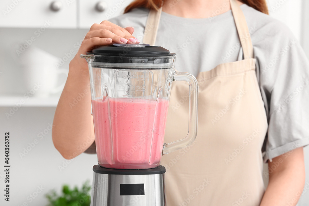 Woman preparing tasty strawberry smoothie with blender in kitchen