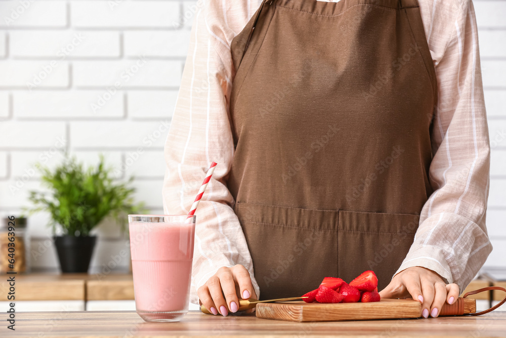 Woman with glass of tasty strawberry smoothie at table in kitchen