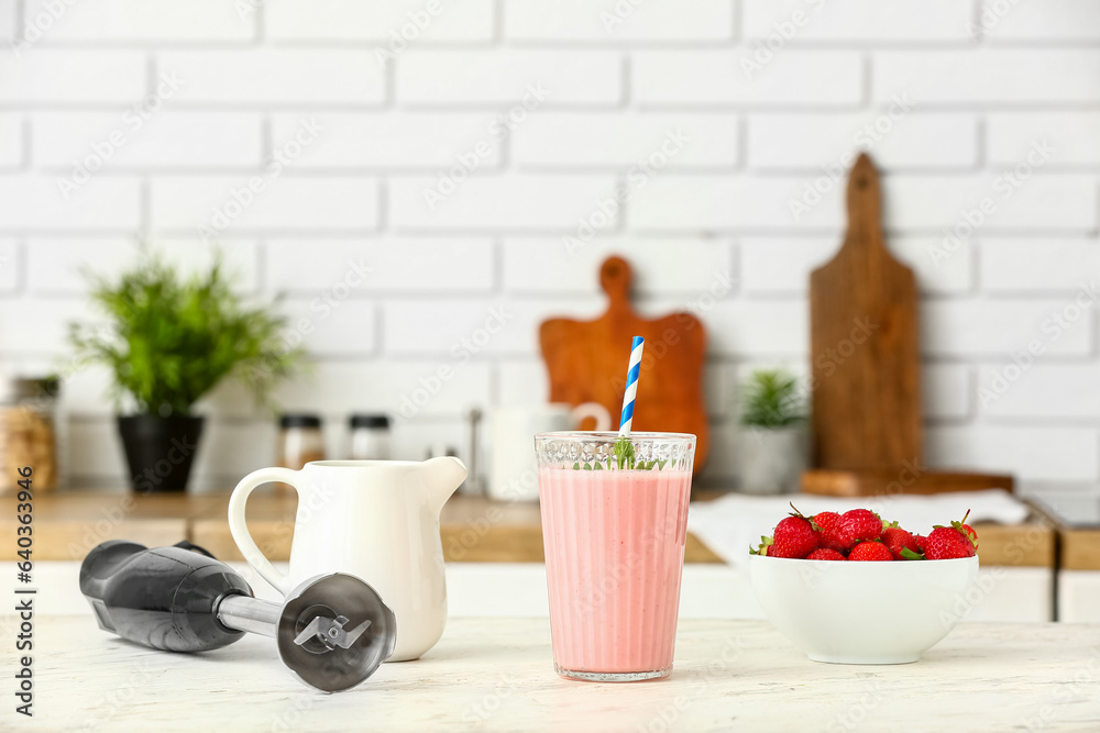 Modern blender and glass of tasty strawberry smoothie on table in kitchen