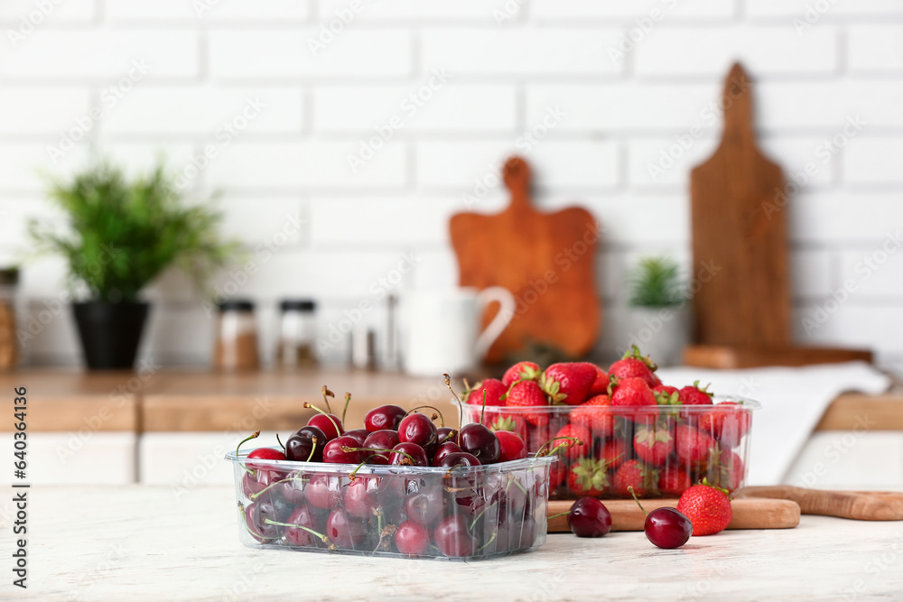 Plastic containers with fresh berries on table in kitchen