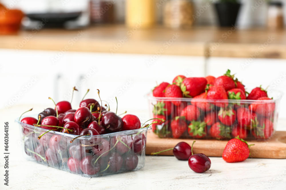 Plastic containers with fresh berries on table in kitchen