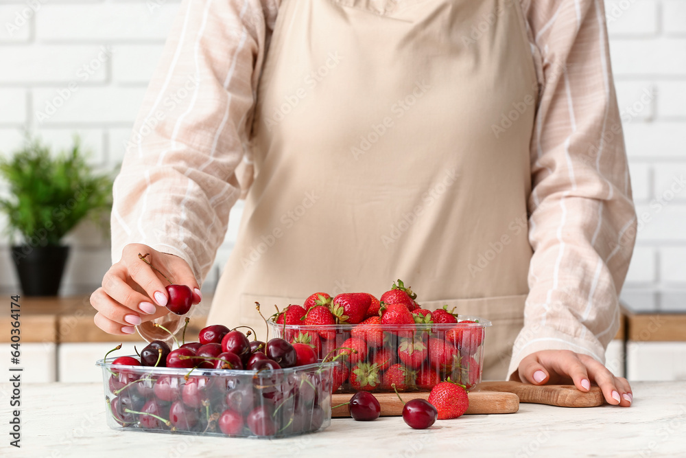 Woman putting ripe berries in plastic containers at table in kitchen