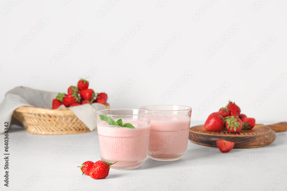 Glasses of tasty strawberry smoothie on light background