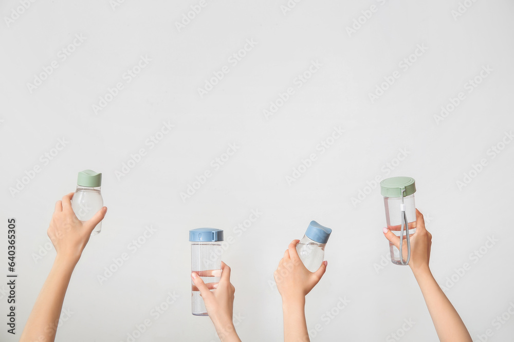 Female hands with bottles of fresh water on light background