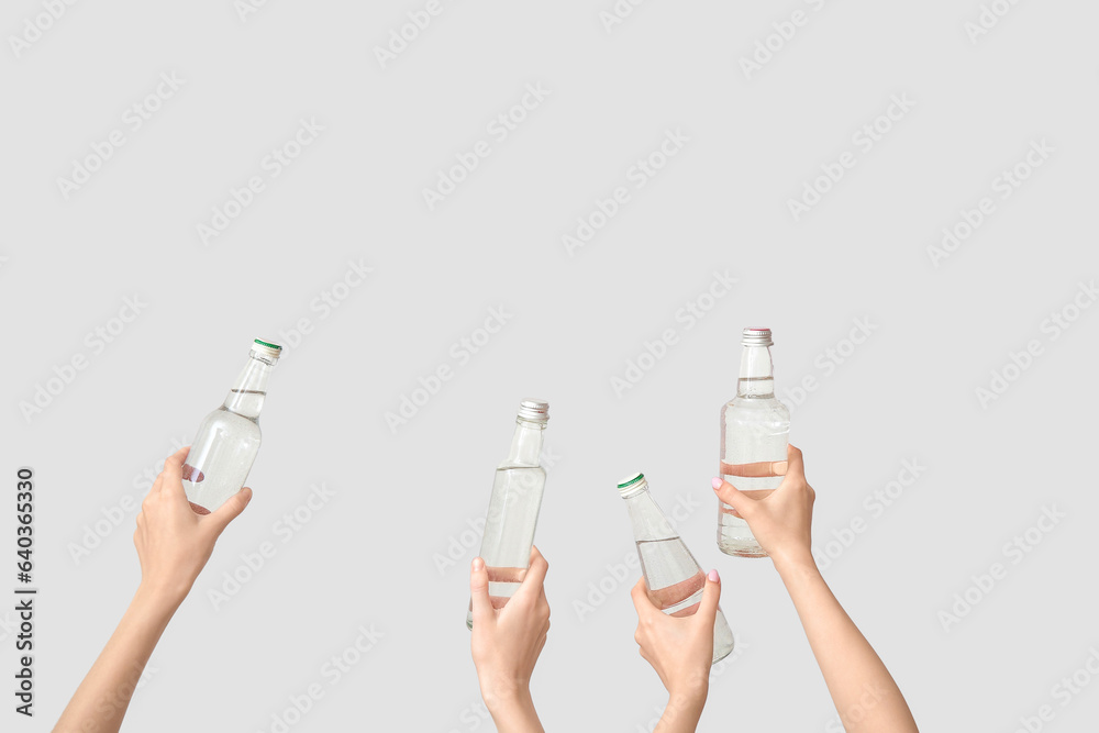 Female hands with bottles of fresh water on light background