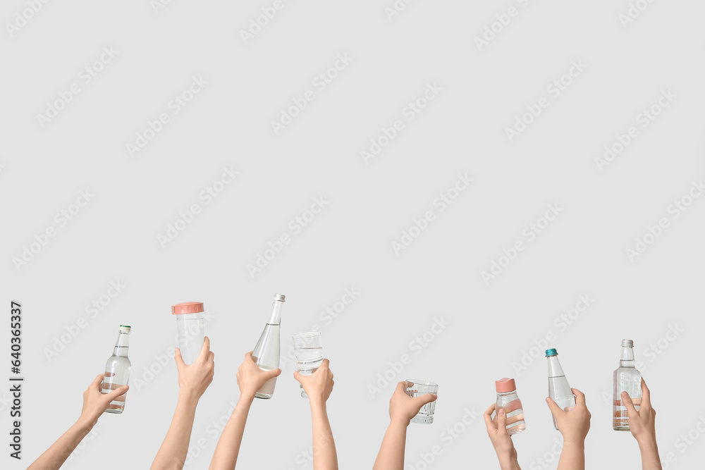 Female hands with bottles and glasses of cold water on light background