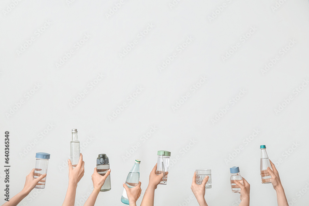 Female hands with bottles and glass of cold water on light background