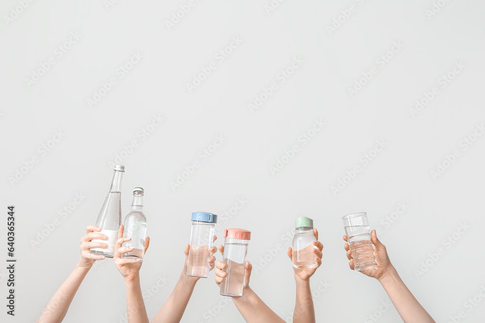 Female hands with bottles of cold water on light background