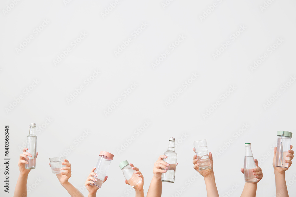 Female hands with bottles and glasses of cold water on light background